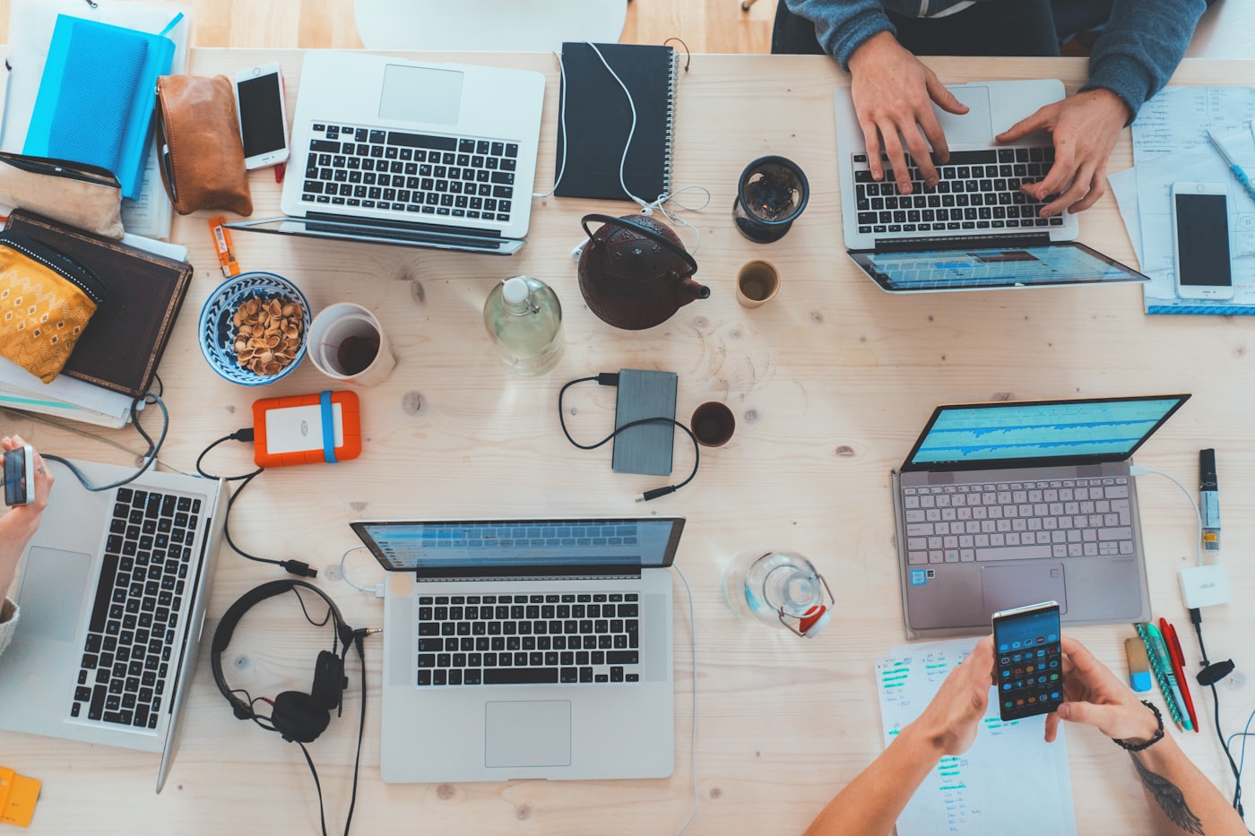 A team's desk seen from above, covered in laptops, notes, and devices