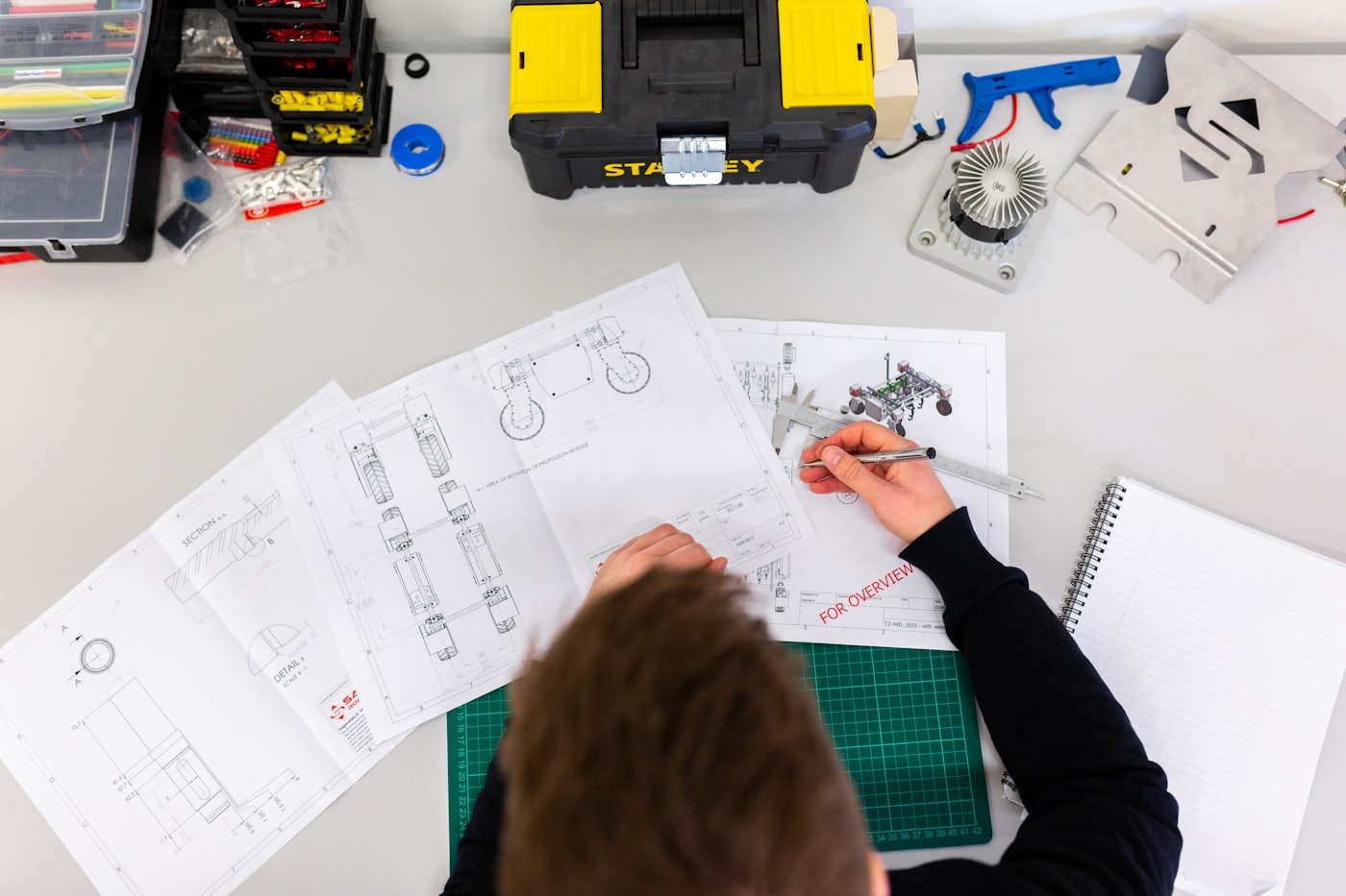 An engineer measuring parts over technical drawings of a machine design
